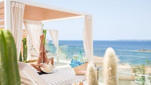 Un área de descanso al aire libre con vistas al mar, con un toldo blanco, sillones y cactus.