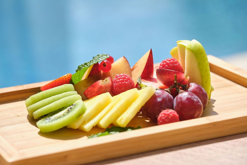 En træbakke med frugtskiver, heriblandt kiwi, ananas, jordbær, hindbær og druer.