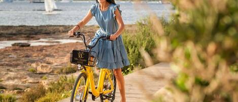 A person riding a yellow bicycle on a wooden boardwalk by a body of water with a sailboat in the background.