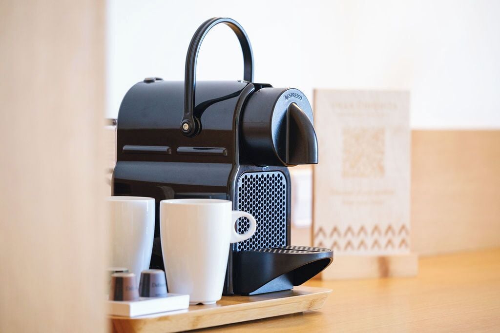 A black espresso machine on a wooden tray with two white cups and a box in the background.