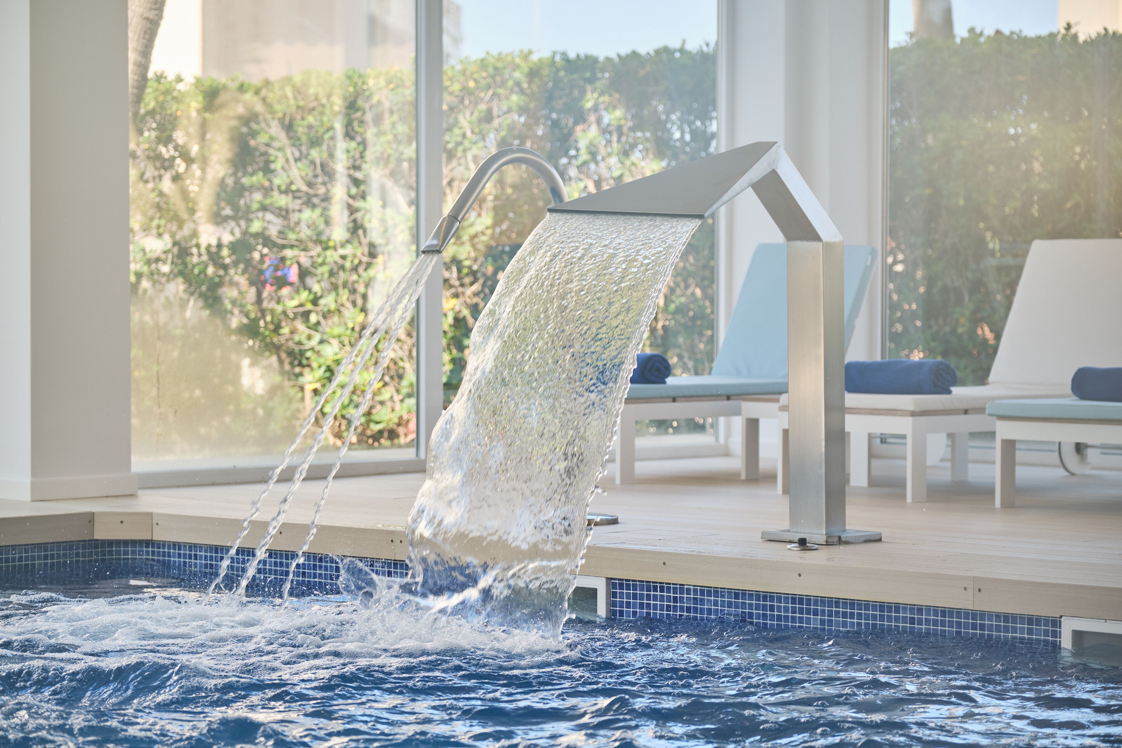 Une piscine dotée d’un élément décoratif aquatique moderne, entourée de chaises longues et offrant une vue sur la verdure.
