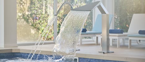 Une piscine dotée d’un élément décoratif aquatique moderne, entourée de chaises longues et offrant une vue sur la verdure.
