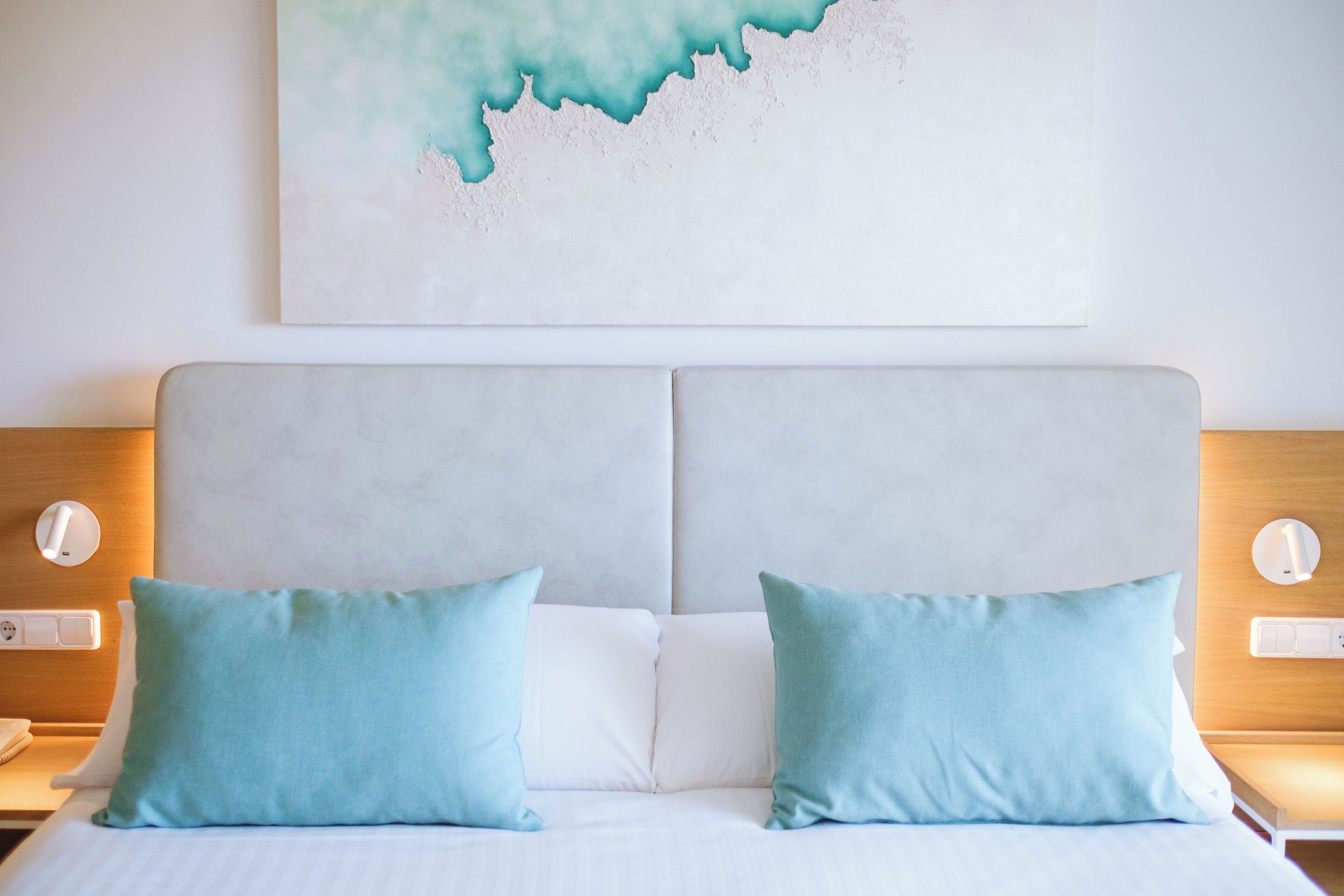 Ein Hotelzimmer mit einem großen Bett, zwei Kissen, einem Kopfteil und einem an der Wand hängenden Kunstwerk.