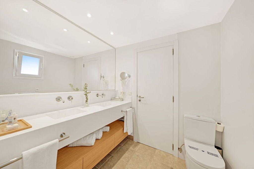 Une salle de bain moderne avec un grand miroir, des éléments en céramique blanche et un meuble-lavabo en bois.