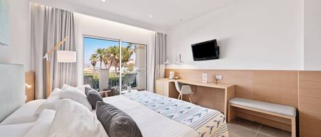 A modern hotel room with a large bed, a desk, a bench, and a TV on the wall.