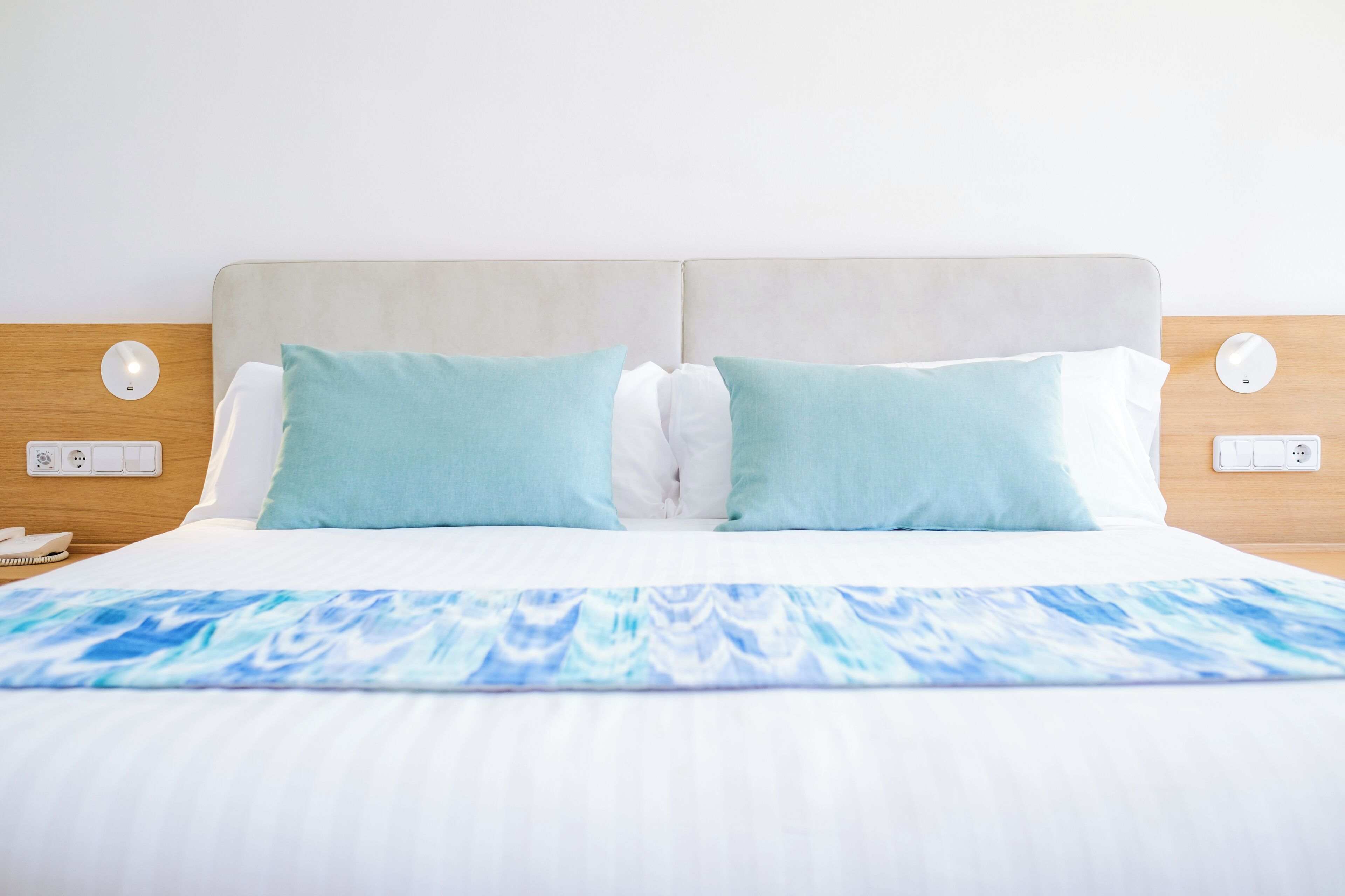 A neatly made bed with a blue and white patterned bedspread, two light blue pillows, and a light-colored headboard.