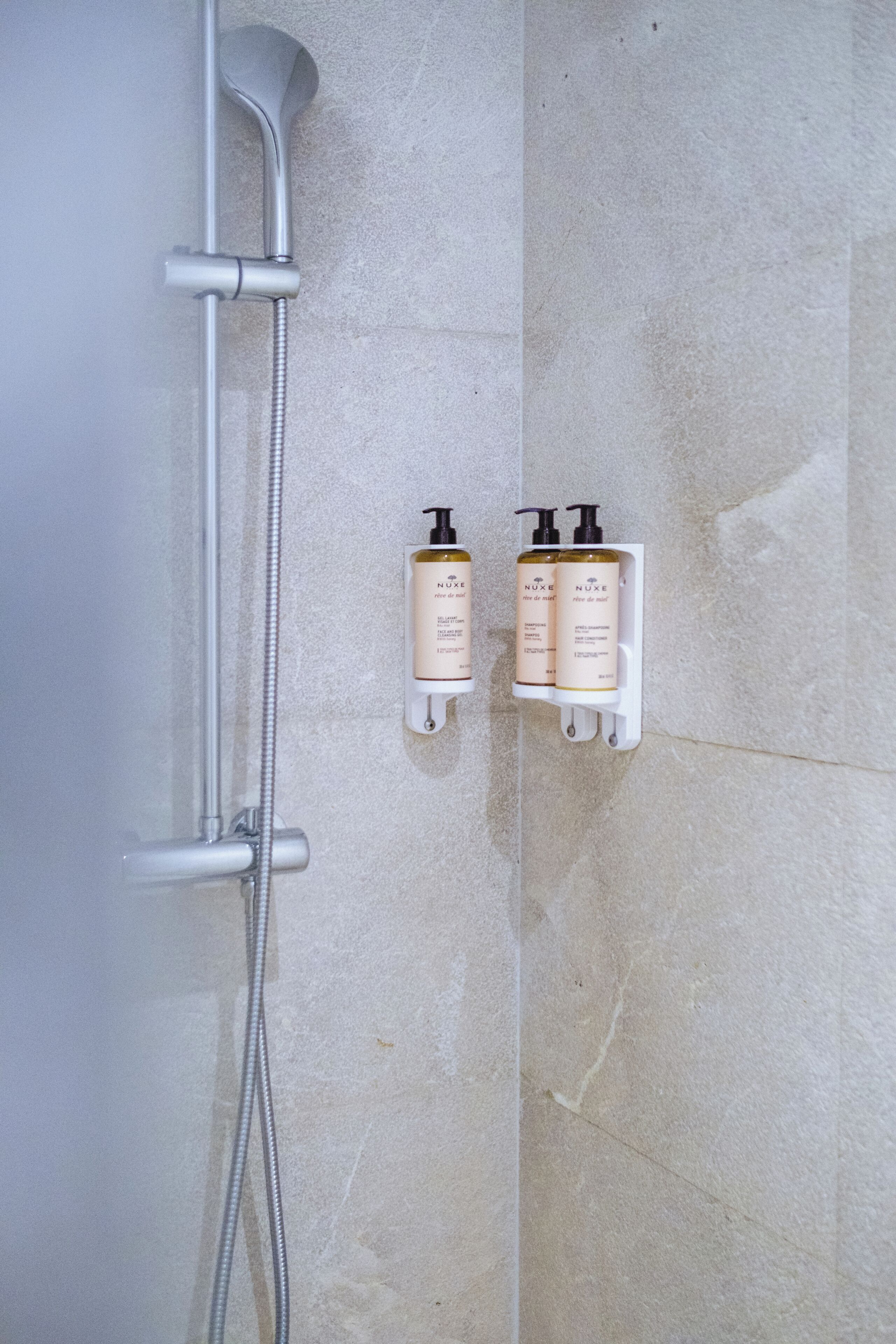A shower with a handheld showerhead and a wall-mounted control panel with two bottles of shampoo.