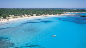 Vista aérea de una playa con aguas azules cristalinas, un bote y un área boscosa al fondo.