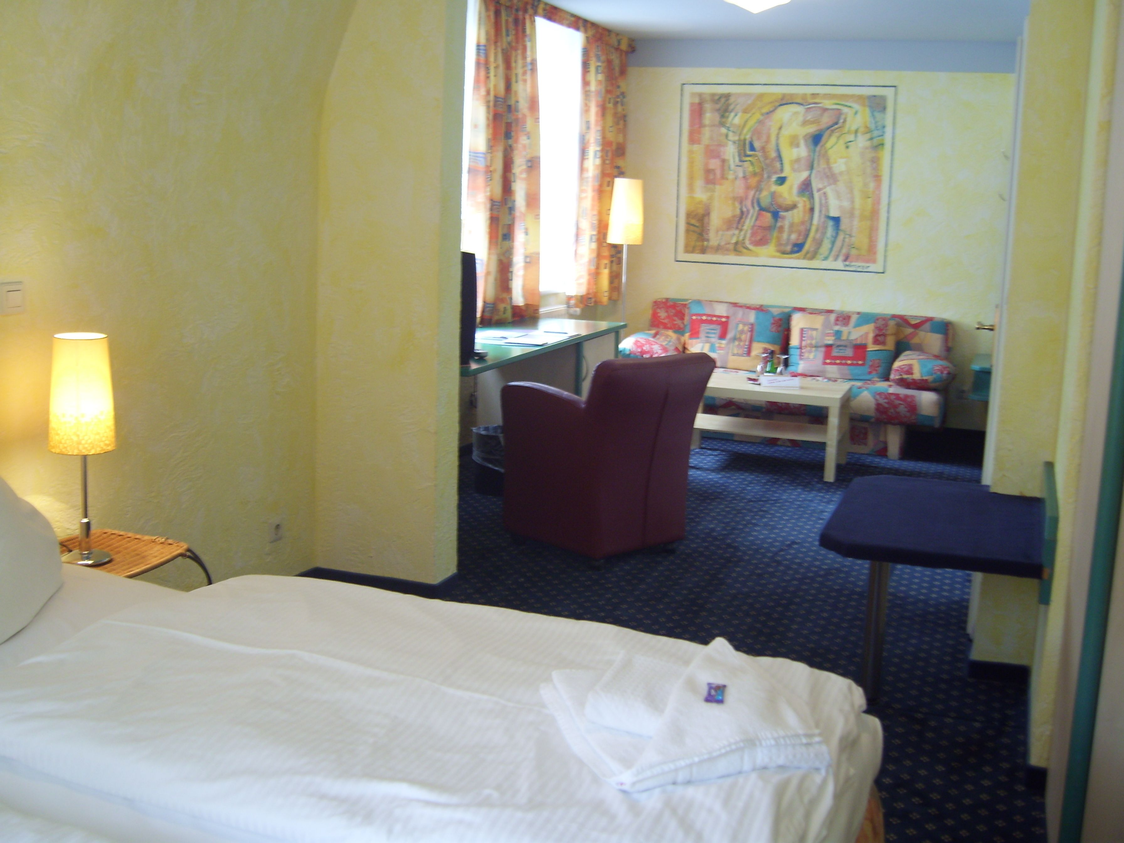 A hotel room with a bed, a desk, a chair, and a sofa.