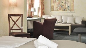 Habitación de hotel con cama, escritorio con lámpara, silla, sofá y un cuadro abstracto grande en la pared.