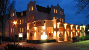 Un hotel de estilo arquitectónico europeo clásico, con una entrada destacada, señalización iluminada y fachada bien iluminada.