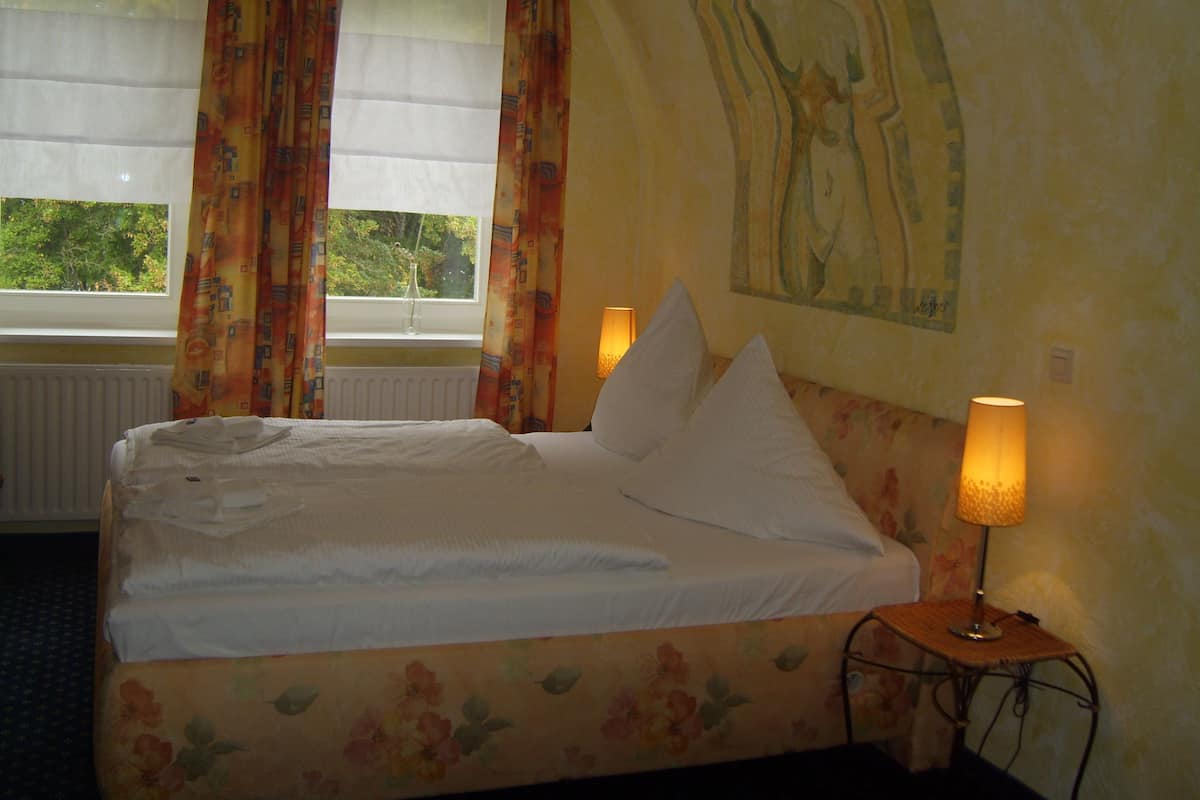Ein Bett mit weißen Bettwäsche, einem Kopfstück mit Blumenmuster und einer Nachttischlampe.