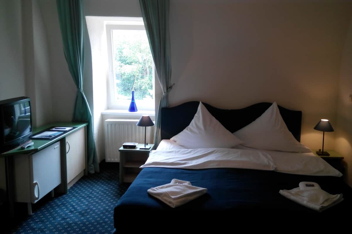 Ein Hotelzimmer mit Bett, Schreibtisch, Computer, Lampe und einem Fenster mit Vorhängen.