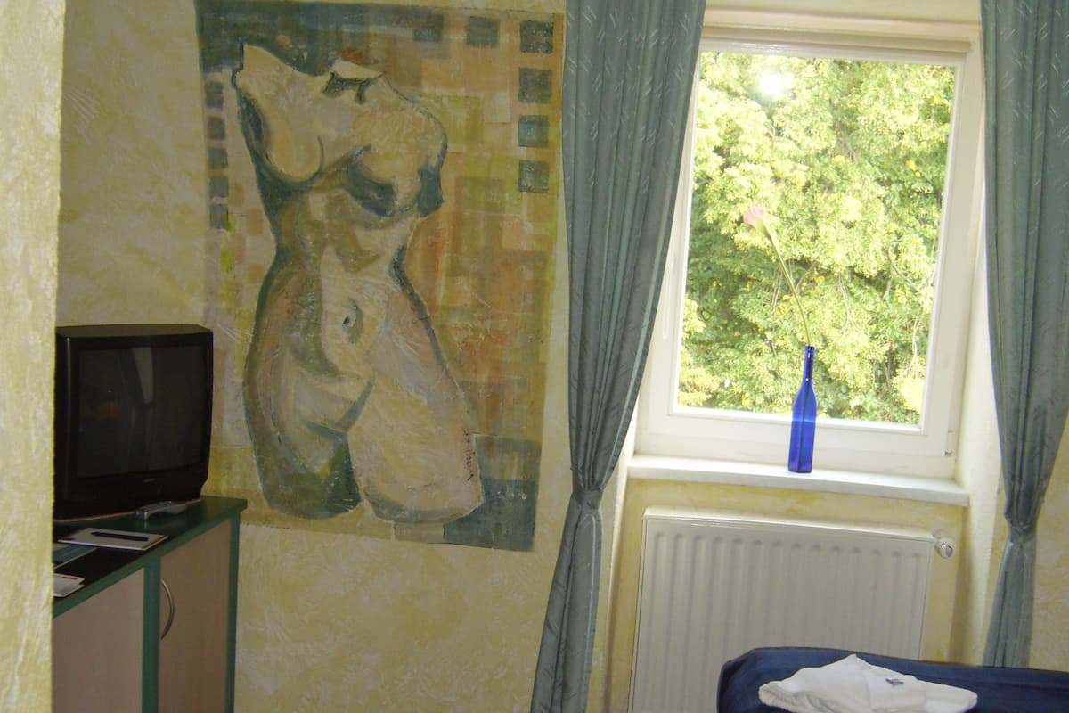 Ein Zimmer mit einem Bett, einem Fernseher, einem Gemälde an der Wand und einem Fenster mit Vorhängen.
