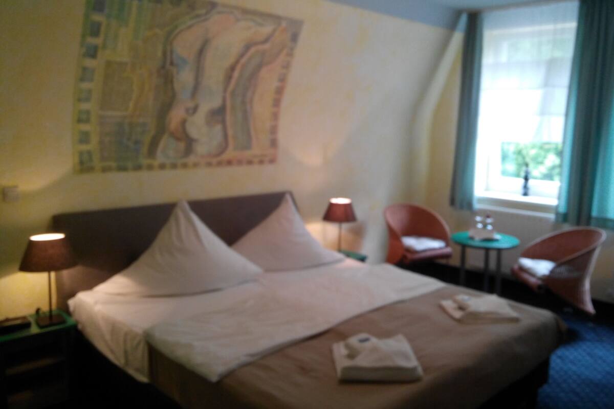 Ein Hotelzimmer mit einem Bett, zwei Stühlen, einem kleinen Tisch und einem Fenster mit Vorhängen.