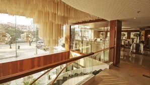 Un moderno vestíbulo de hotel con una escalera de cristal, vistas a la calle y una zona de recepción con mostrador y asientos.