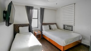 A hotel room with two single beds, a TV mounted on the wall, a window with curtains, and a built-in air conditioning unit. - Midtown West Hotel (New York)
