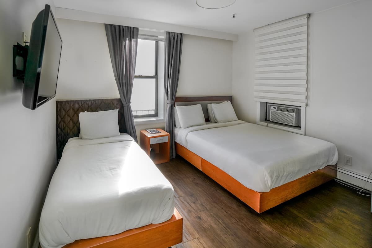 Een hotelkamer met twee eenpersoonsbedden, een aan de muur bevestigde televisie, een raam met gordijnen en een ingebouwde airconditioning.
