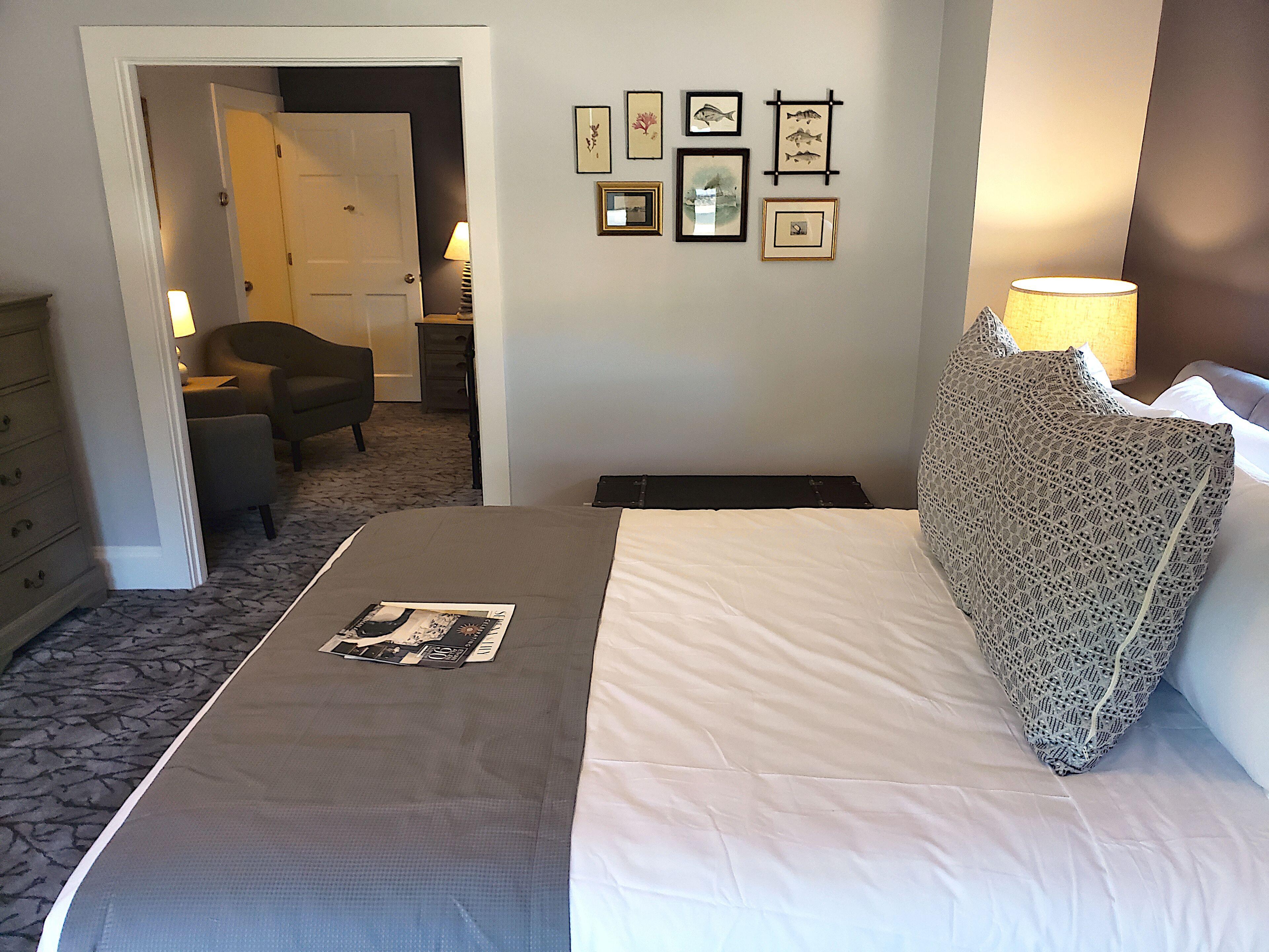 A neatly arranged hotel room with a bed, a chair, a dresser, and a wall with framed pictures.