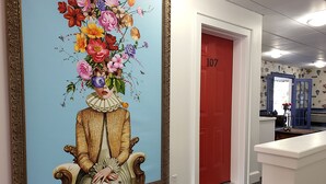 A hallway with a large floral painting, a red door labeled 107, and a blue patterned wall. - Little Fig Hotel (Bar Harbor)