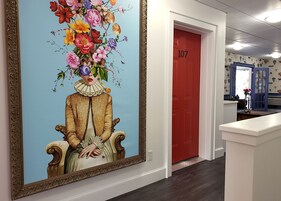 A hallway with a large floral painting, a red door labeled 107, and a blue patterned wall.