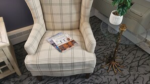 A plaid armchair with magazines, a small table with a plant, and a radiator in a room with patterned carpet. - Little Fig Hotel (Bar Harbor)