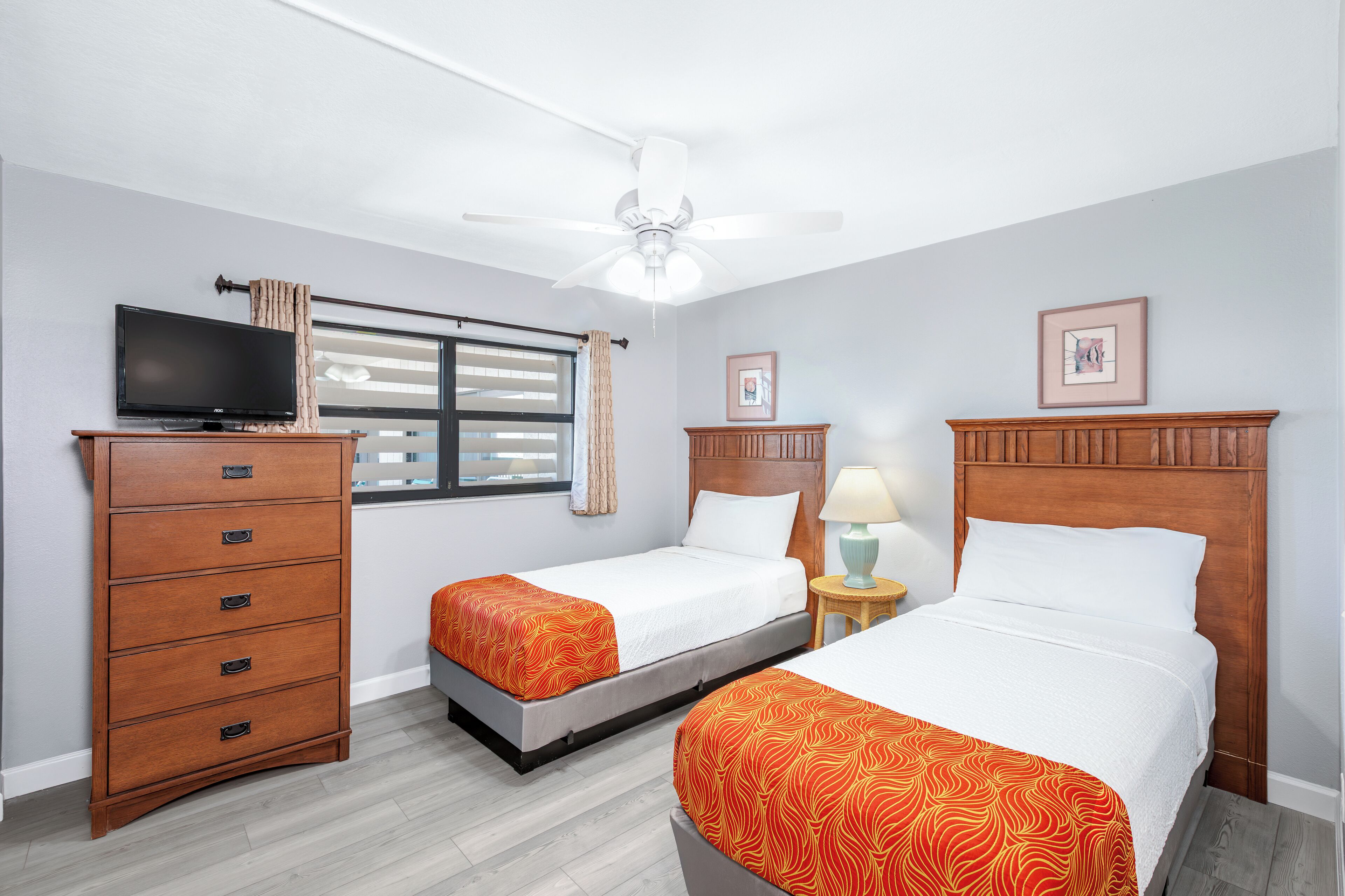 A hotel room with two beds, a dresser, a television, and a window with curtains.