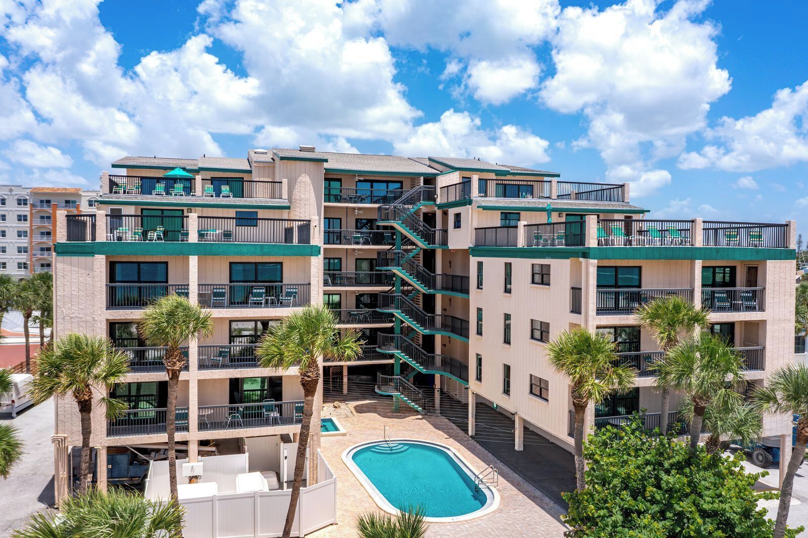 A multi-story hotel with balconies, a swimming pool, and palm trees.