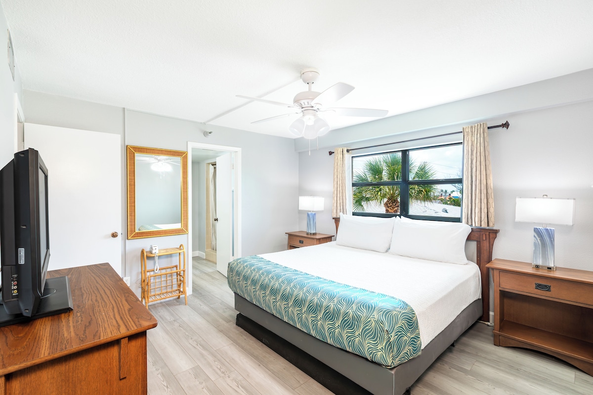 Habitación de hotel con cama, televisor, escritorio y ventana con cortinas.