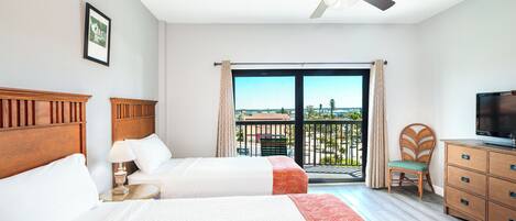Habitación de hotel con dos camas, televisor, ventilador de techo y balcón con vistas.
