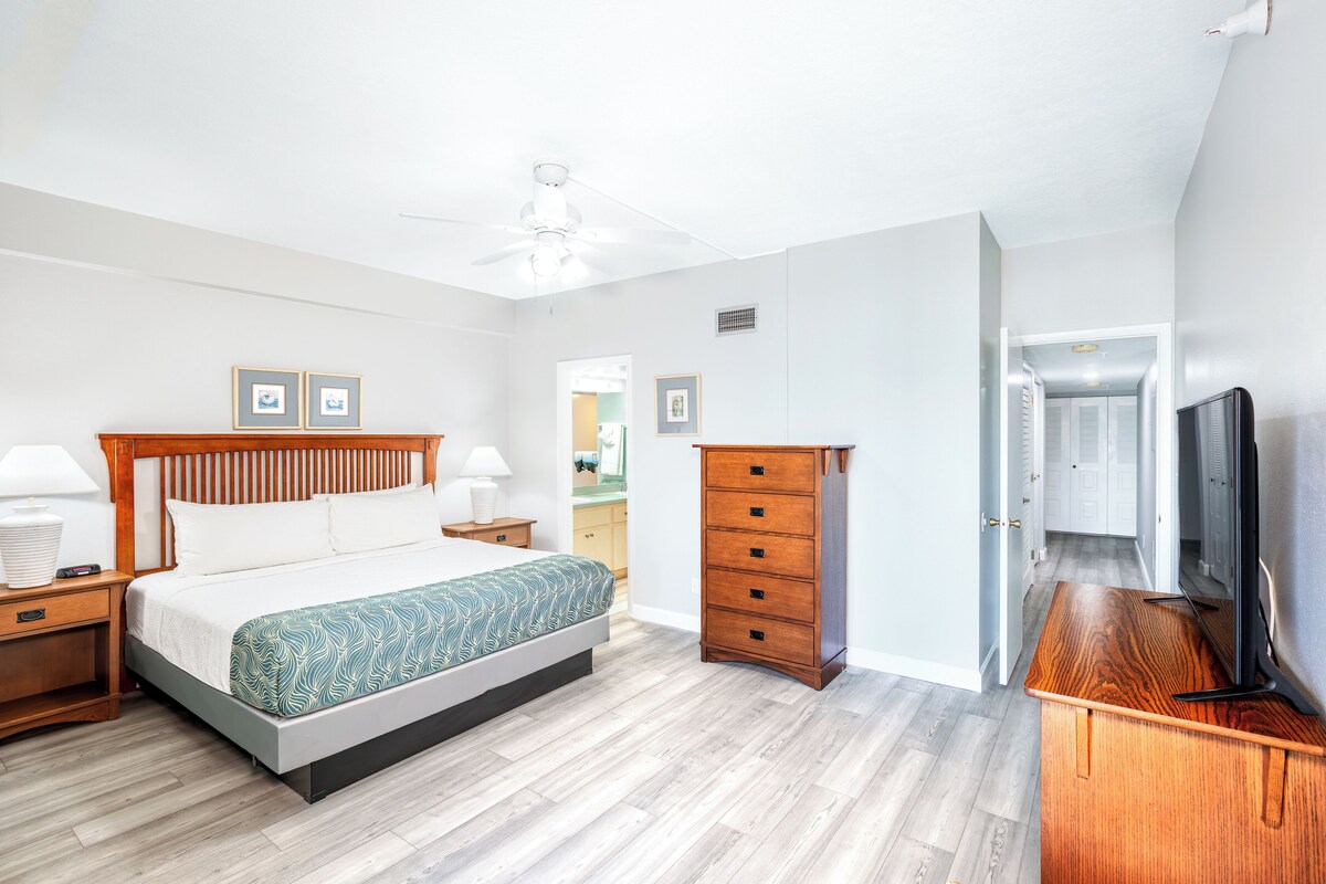 Un dormitorio con cama, cómoda de madera, mesitas de noche y televisor.