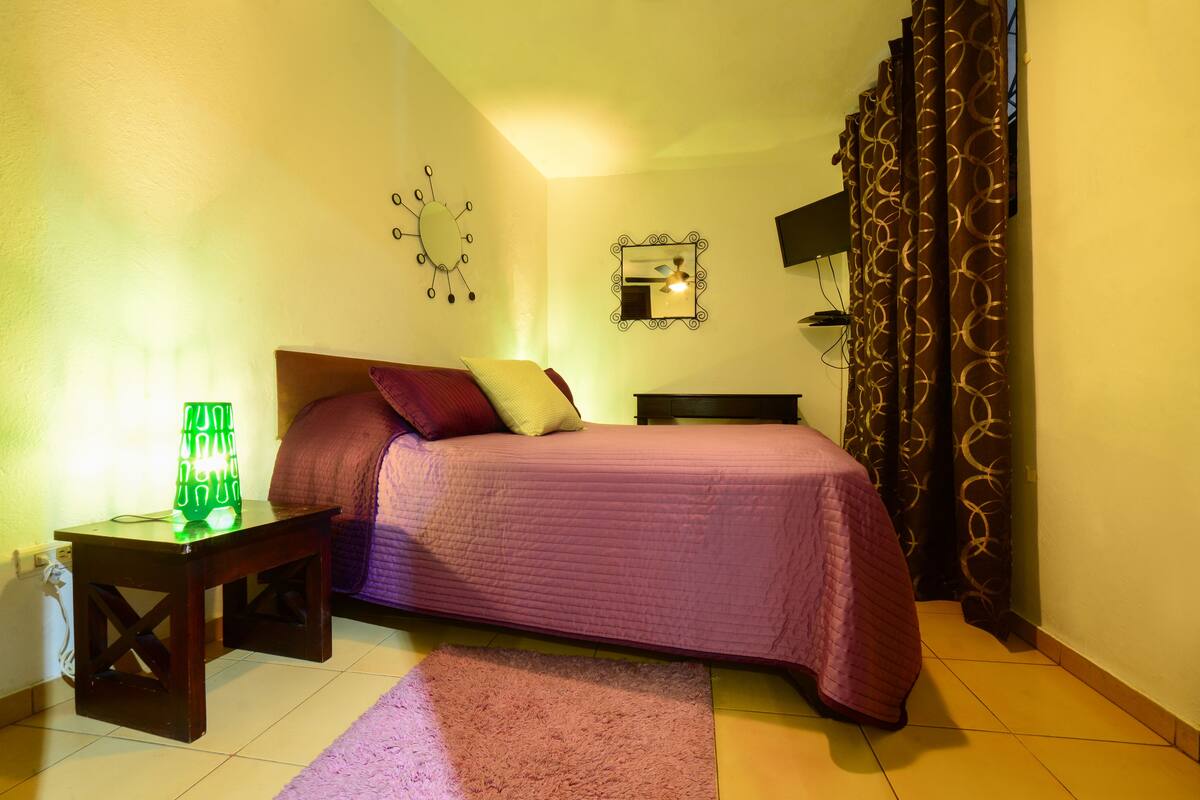 Une chambre à coucher avec un lit, une table de chevet, une lampe, un miroir et des rideaux.