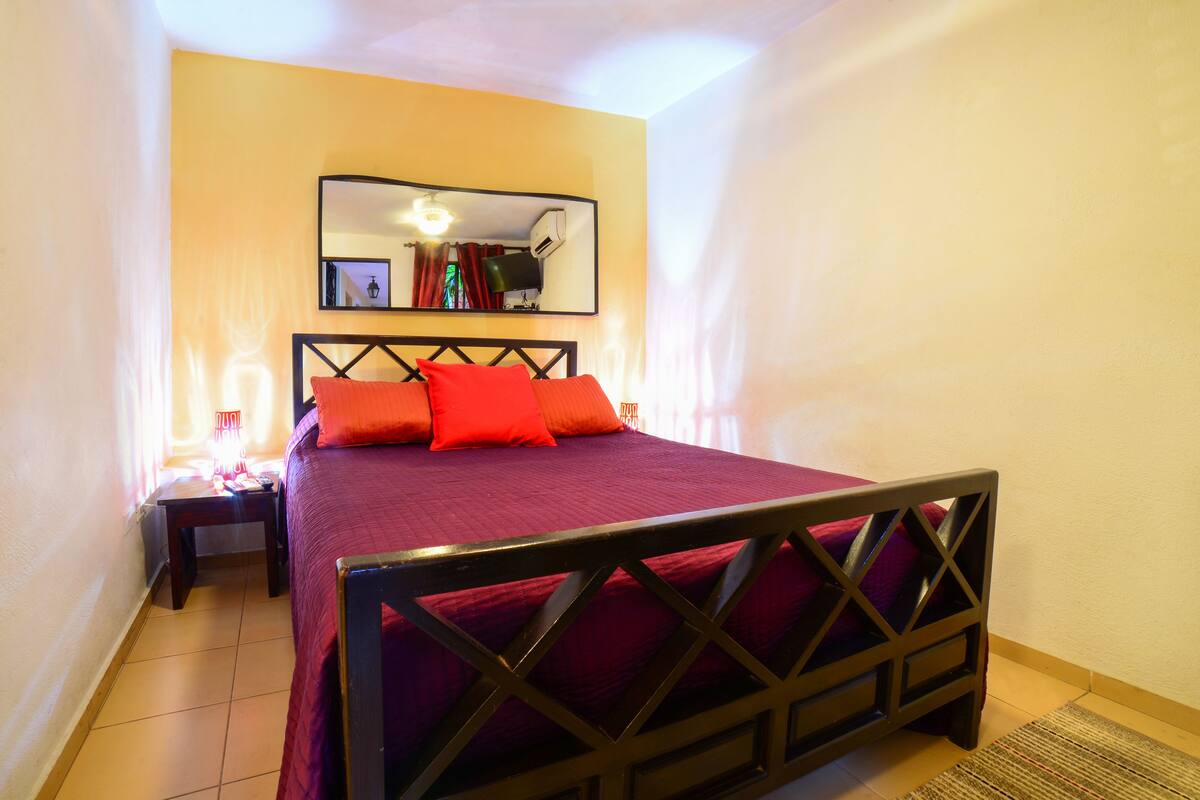 Une chambre à coucher comprenant un lit, une table de chevet, un miroir et un climatiseur fixé au mur.