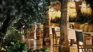 Un espacio de comedor al aire libre con mesas y sillas, rodeado de follaje y pilares de piedra.