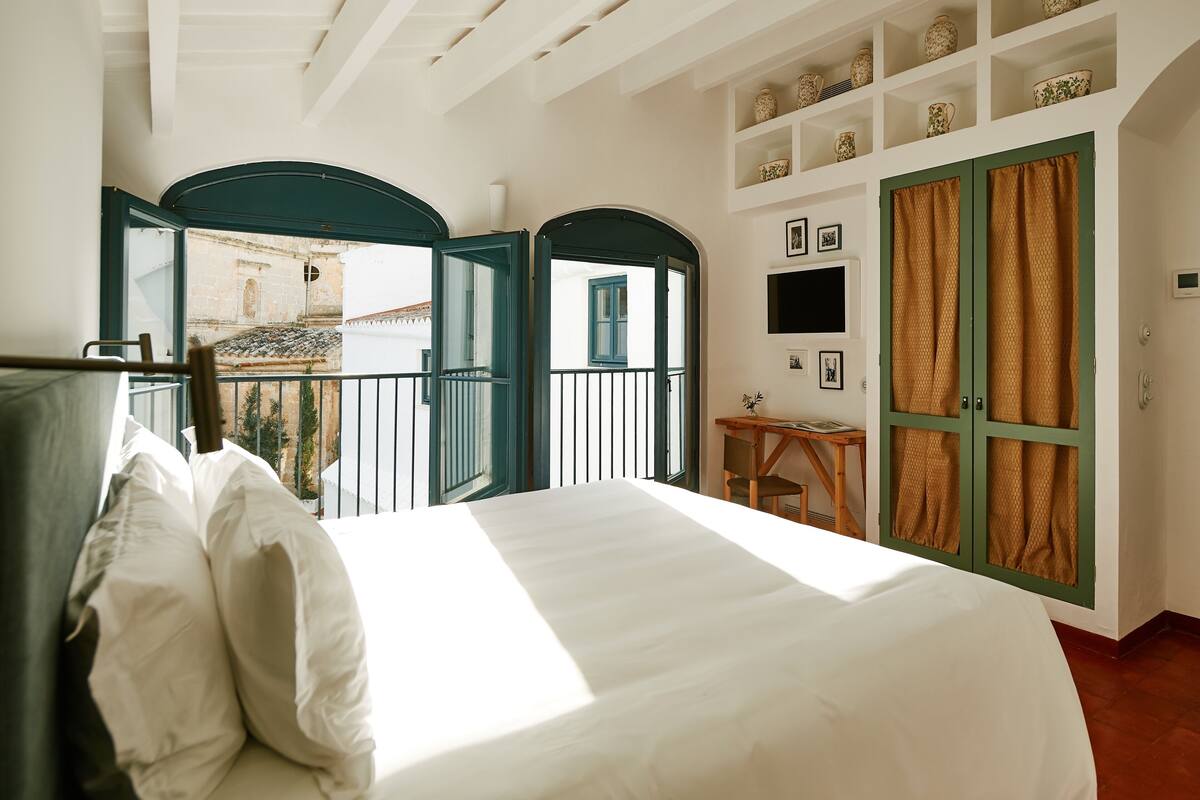 A bedroom with a large bed, a small table, and a view of the outside.