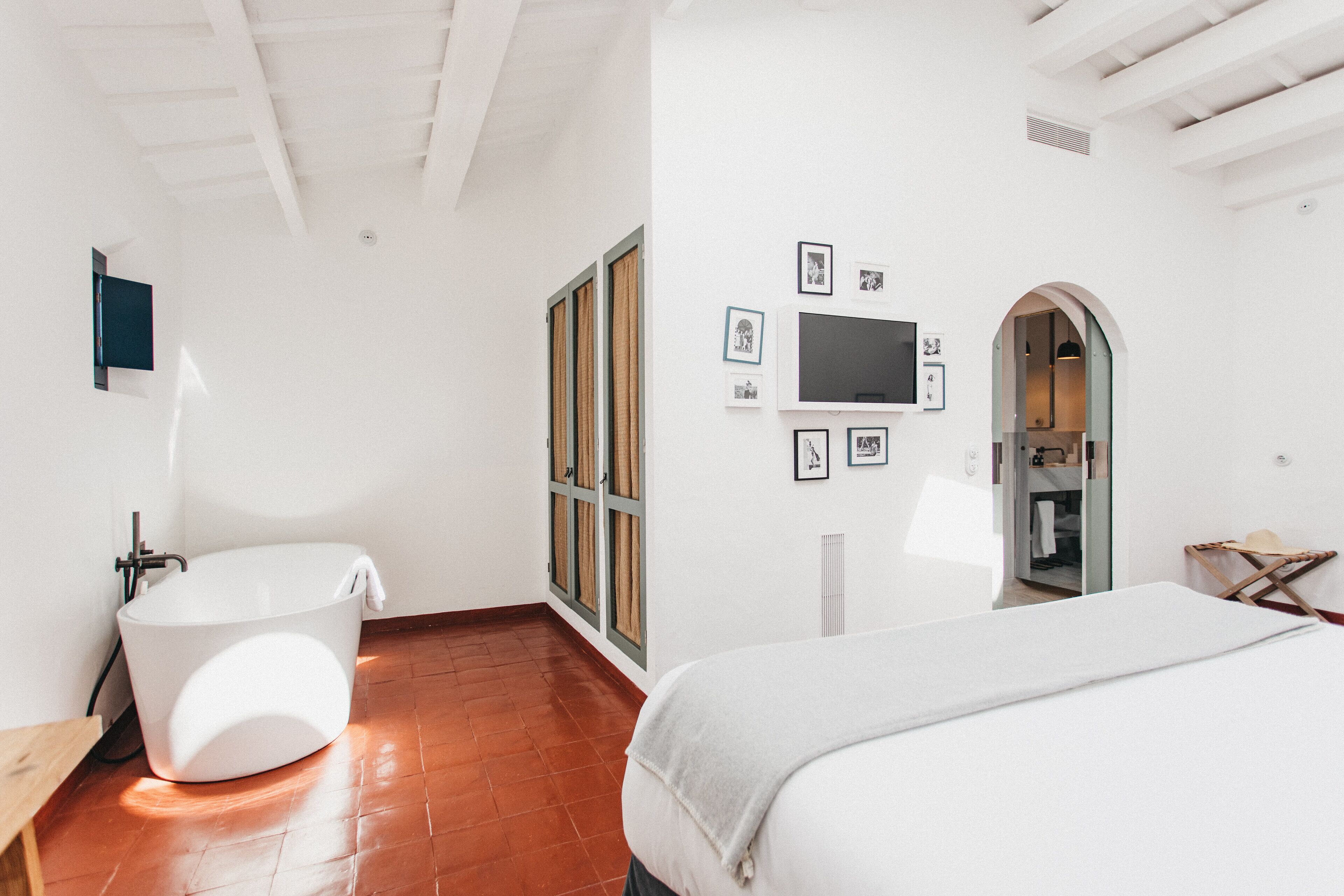 Un dormitorio moderno con una cama grande, una bañera y un televisor en la pared.