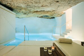 Un cuarto de spa con techo de piedra, una bañera de hidromasaje, un banco de madera y una mesa con velas.