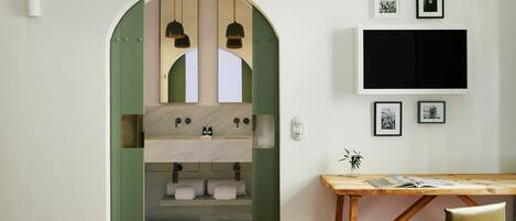 A modern bathroom with a green archway, a wooden desk with a chair, and a flat-screen TV mounted on the wall.