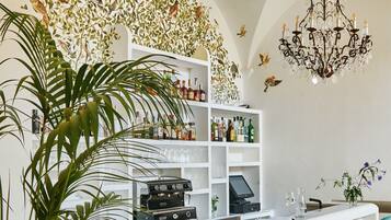 Una zona de bar con una barra blanca, taburetes azul turquesa, una máquina de café y una pared con un mural de aves.