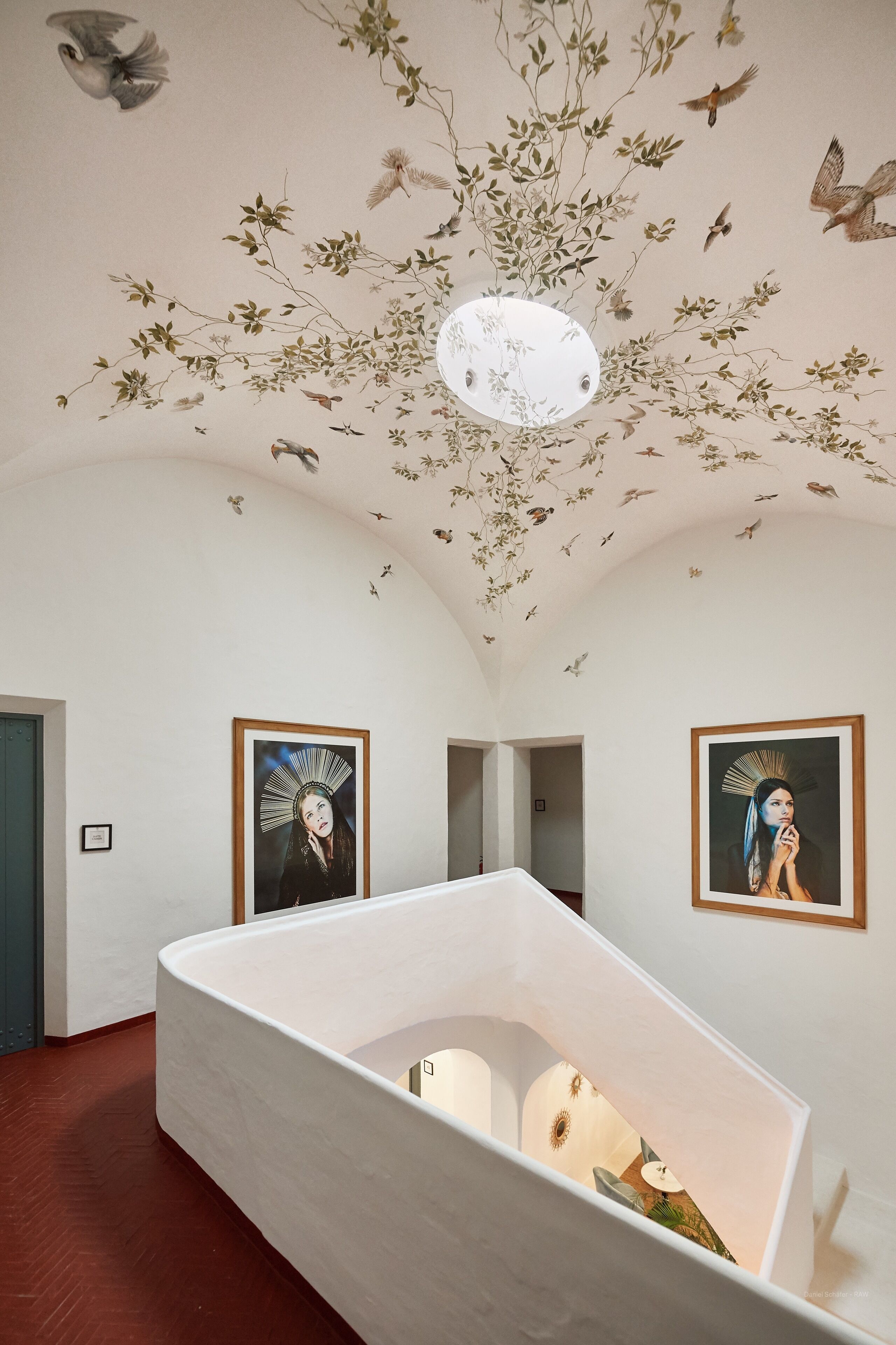 A room with a white bathtub, two framed artworks on the walls, and a ceiling with bird and plant motifs.
