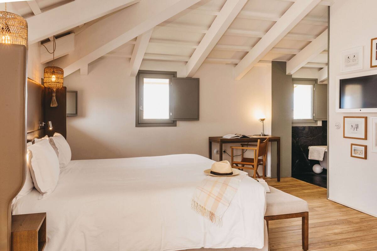 A bedroom with a large bed, a desk, and a bathroom visible through an open door.