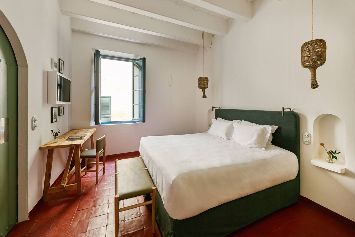 A bedroom with a green bed, a wooden desk, a chair, and a small shelf with a plant.