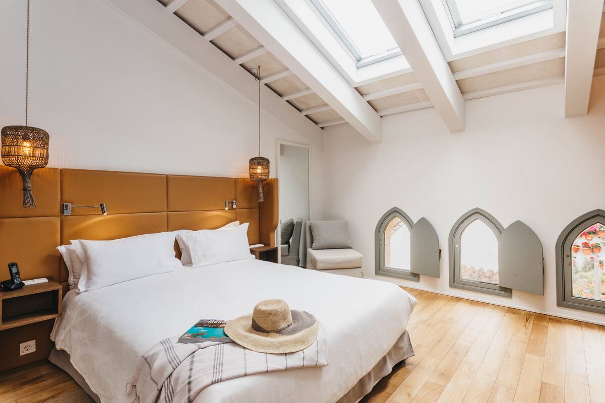 A modern bedroom with a large bed, a skylight, and a view of the garden through arched windows.