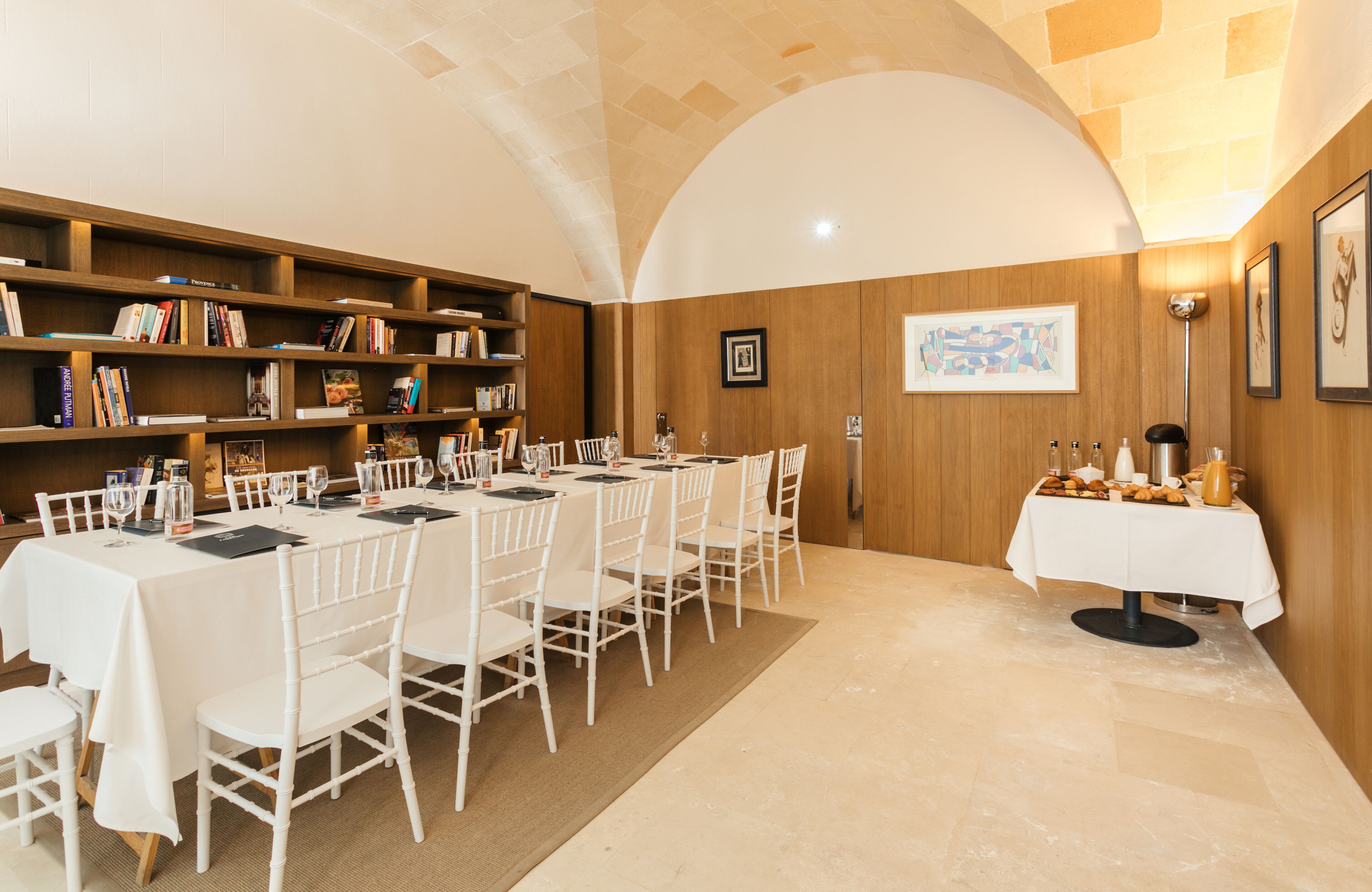 A dining area with a long table set for a meal, surrounded by bookshelves and a wooden wall.