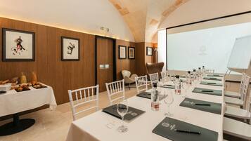 Un salón de conferencias con una larga mesa preparada para una reunión, obras de arte enmarcadas en las paredes y una pantalla de proyector.
