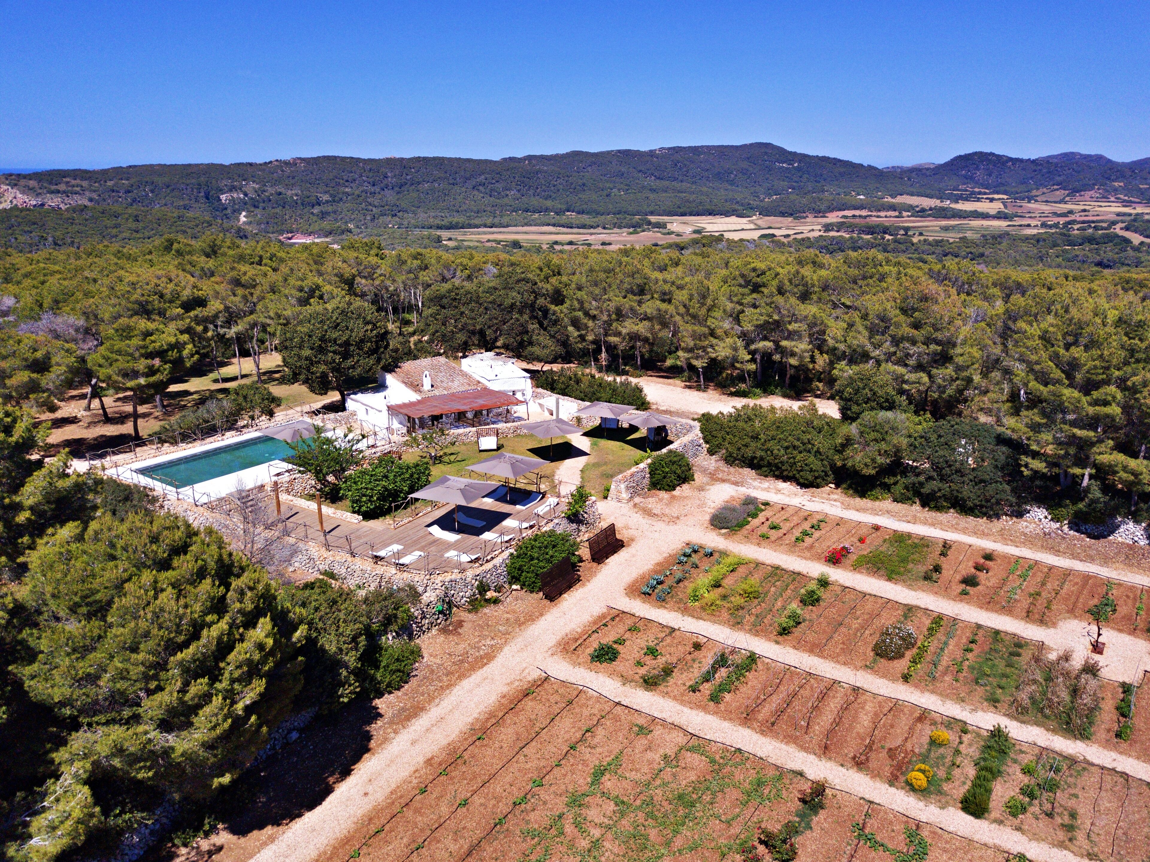 An aerial view of a property with a swimming pool, outdoor seating area, and terraced gardens.