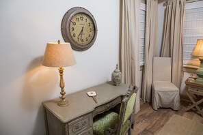 Un escritorio de estilo antiguo con una lámpara, un reloj y una silla en una habitación con suelo de madera y cortinas.