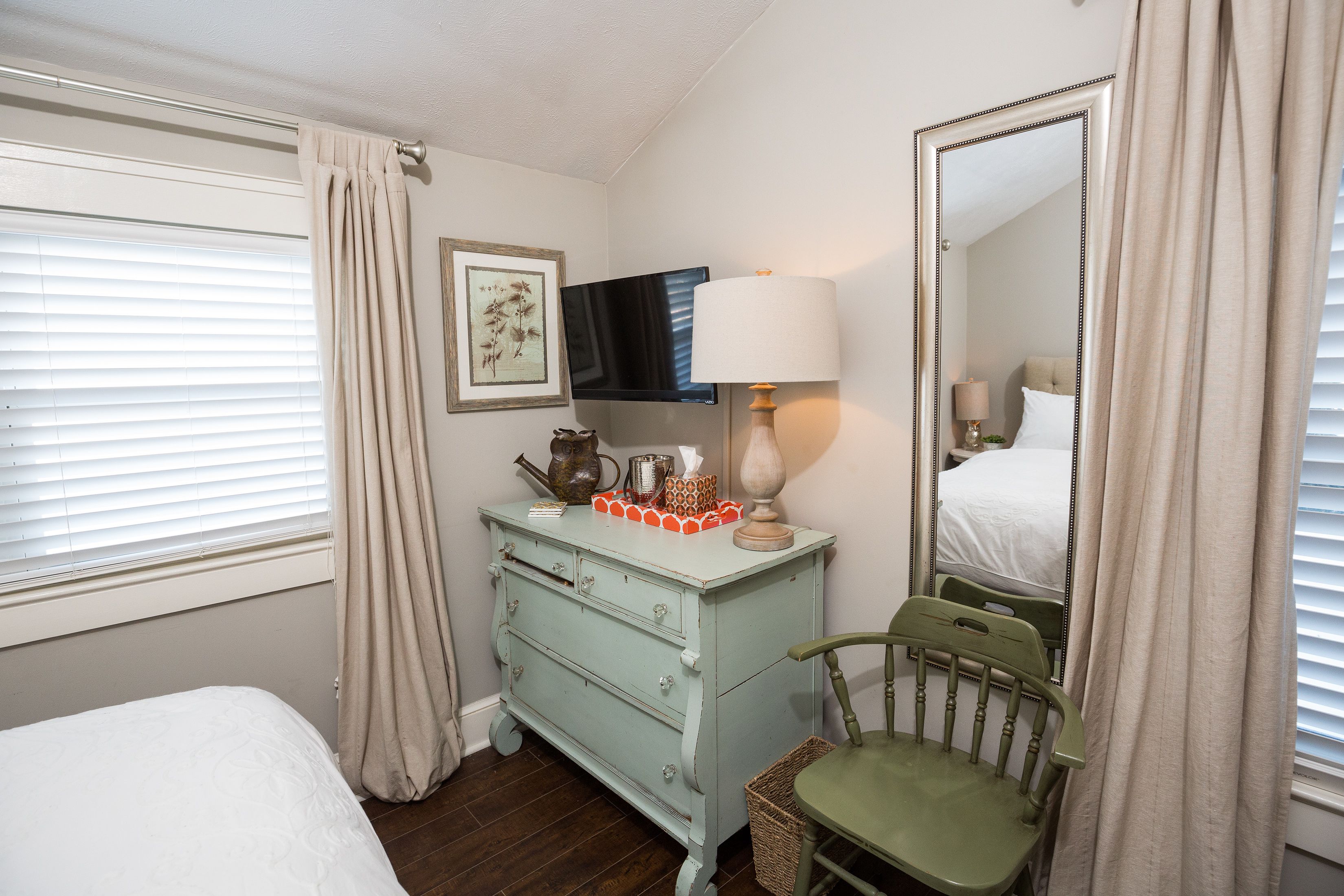 A bedroom with a bed, a dresser, a chair, a mirror, and a television.