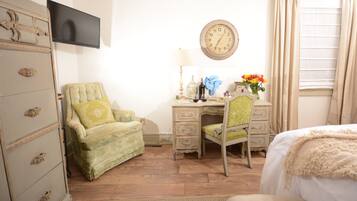 A room with a bed, a desk with a chair, a dresser, a television, a clock, and a window with curtains.