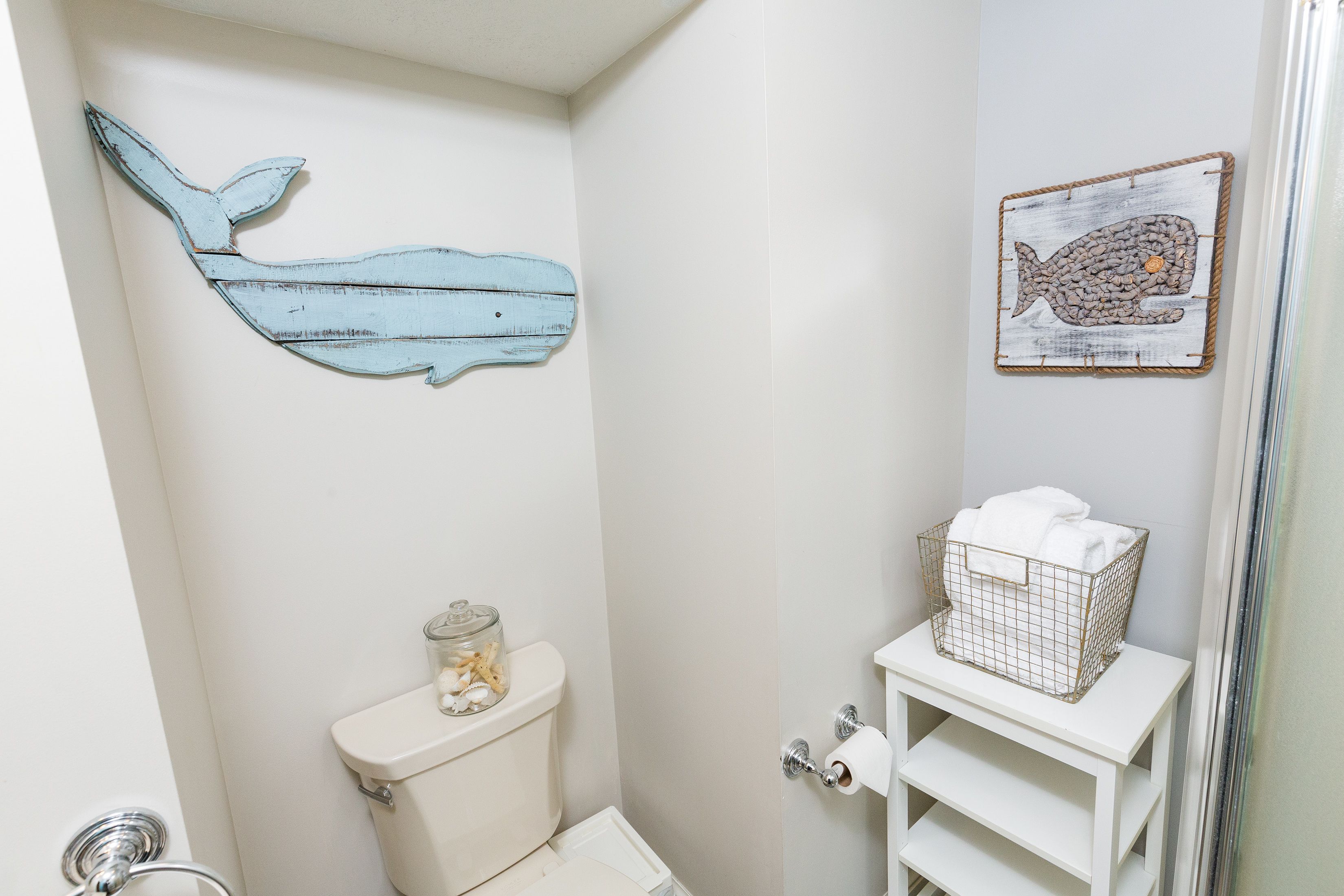 A bathroom with a toilet, a shelf with a basket, and two wall decorations.